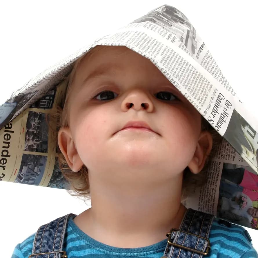 33316_AdobeStock_11521023.jpeg Kind mit einer Zeitung als Hut auf dem Kopf