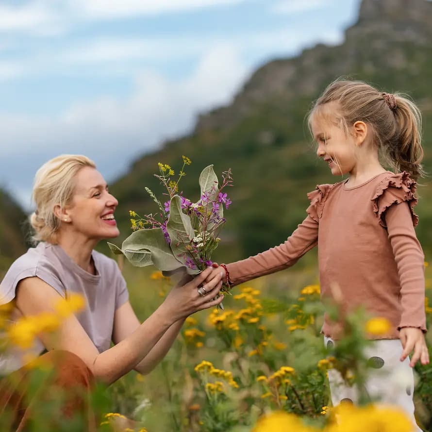101638_SOS-KD_iStock_miniseries_2177876032.jpg Frau und Mädchen auf Wiese, Mädchen reicht Frau einen Blumenstrauß